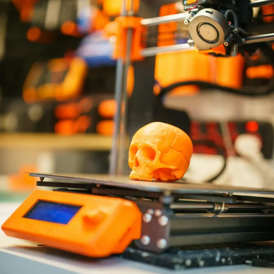 A close-up of an orange 3D printed skull on a 3D printer, showcasing modern technology in a workshop setting.