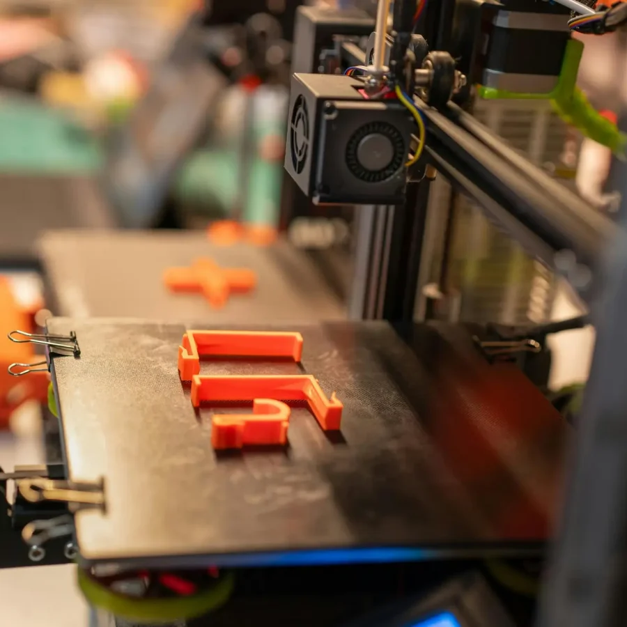 Detailed view of a 3D printer creating an orange plastic part showcasing advanced technology.